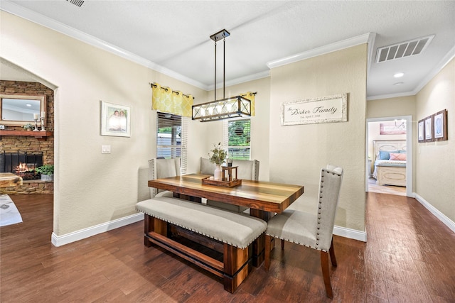 dining space with visible vents, crown molding, baseboards, a stone fireplace, and dark wood finished floors
