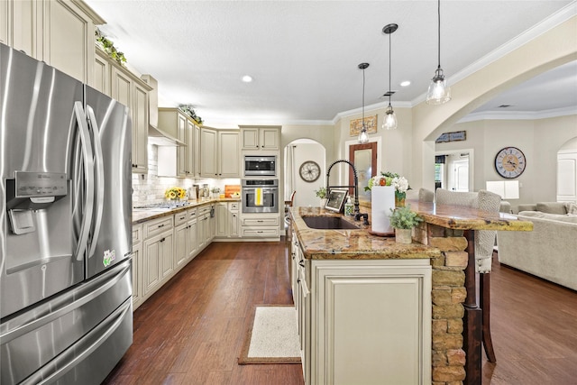 kitchen with dark wood-style flooring, open floor plan, cream cabinetry, a sink, and appliances with stainless steel finishes