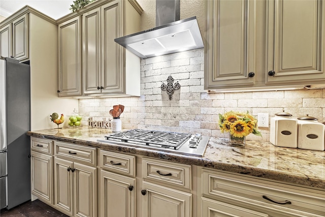 kitchen with appliances with stainless steel finishes, cream cabinetry, wall chimney exhaust hood, and tasteful backsplash