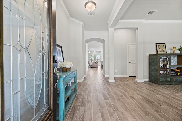 entryway with arched walkways, baseboards, wood finished floors, visible vents, and ornamental molding