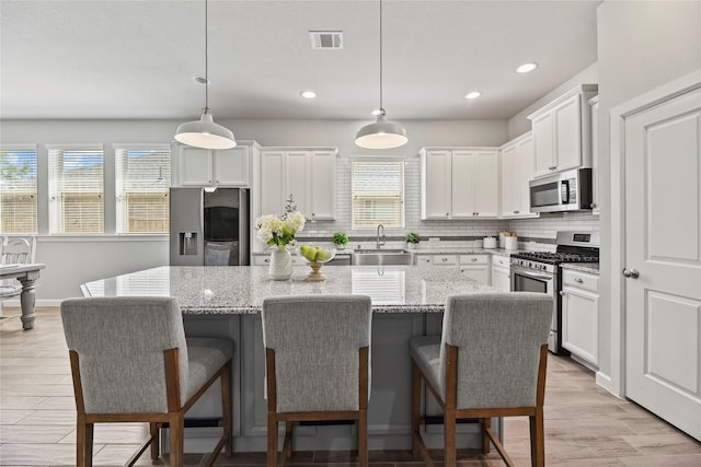 kitchen with decorative backsplash, visible vents, appliances with stainless steel finishes, a center island, and a sink