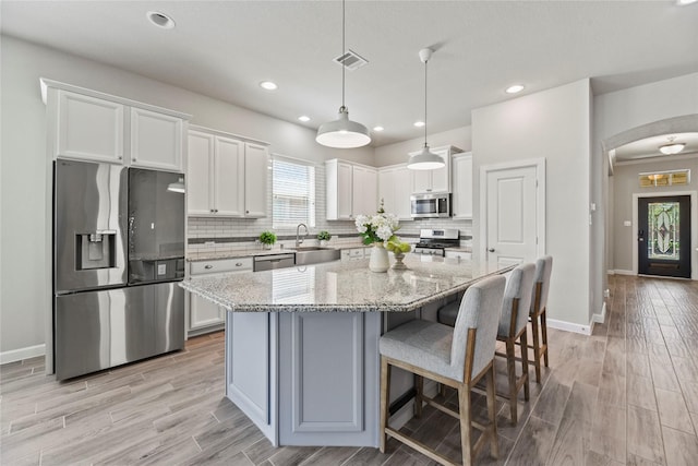 kitchen featuring appliances with stainless steel finishes, arched walkways, a sink, white cabinets, and light wood-style floors
