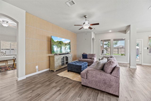 living area featuring ceiling fan, visible vents, arched walkways, wood finished floors, and baseboards