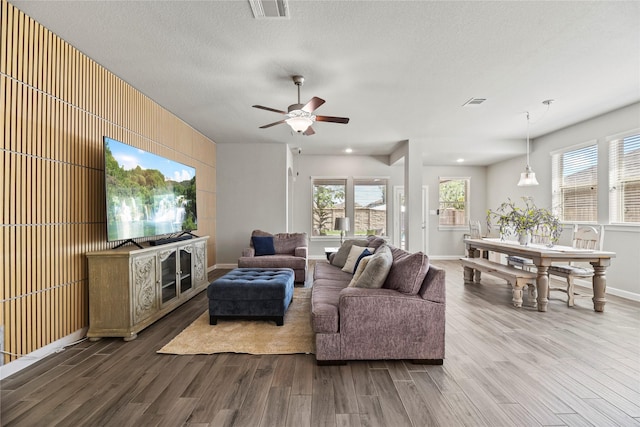 living room with ceiling fan, a textured ceiling, baseboards, wood finished floors, and visible vents