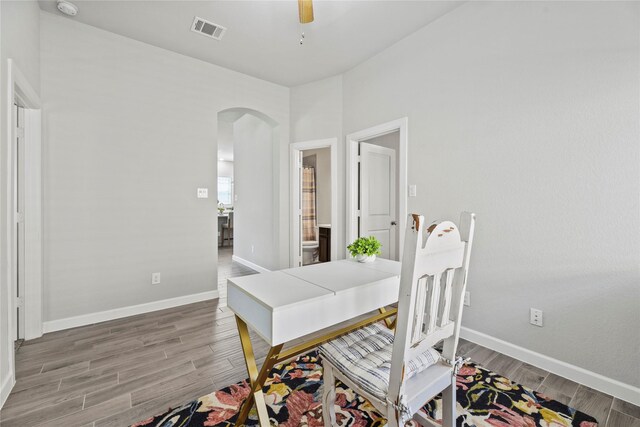 office with arched walkways, a ceiling fan, baseboards, wood finished floors, and visible vents