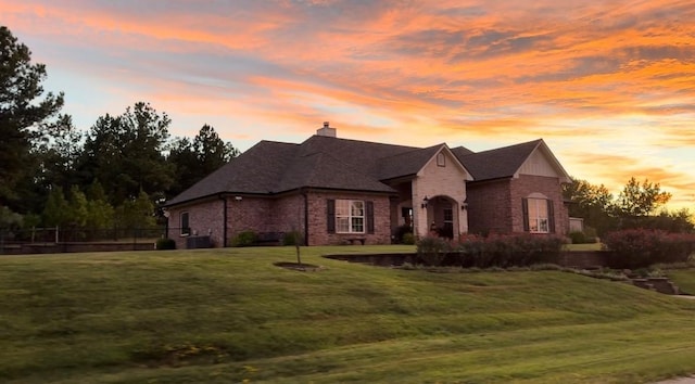 french country inspired facade featuring fence, a chimney, a front lawn, and brick siding
