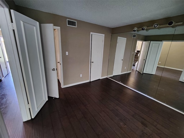 unfurnished bedroom featuring visible vents, a textured ceiling, dark wood finished floors, and baseboards