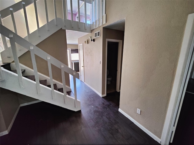 stairway with visible vents, a textured wall, wood finished floors, baseboards, and a high ceiling