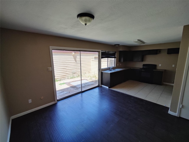 kitchen with a textured ceiling, black electric range, a sink, baseboards, and light wood finished floors