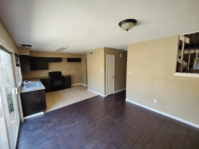 unfurnished living room featuring a sink, a textured ceiling, baseboards, light wood-type flooring, and visible vents