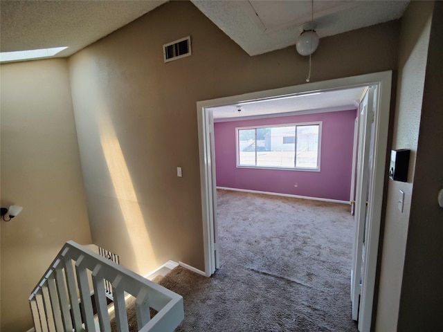 hall with visible vents, baseboards, carpet floors, and an upstairs landing