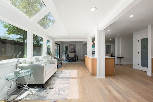 living room featuring a skylight, baseboards, recessed lighting, and light wood-style flooring