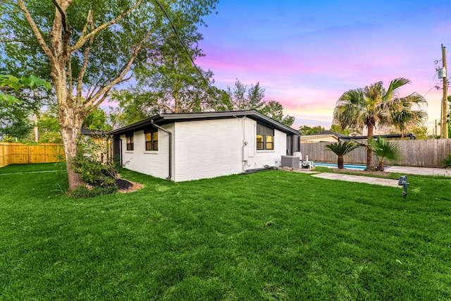 back of house at dusk with a lawn, a fenced backyard, central air condition unit, and a fenced in pool