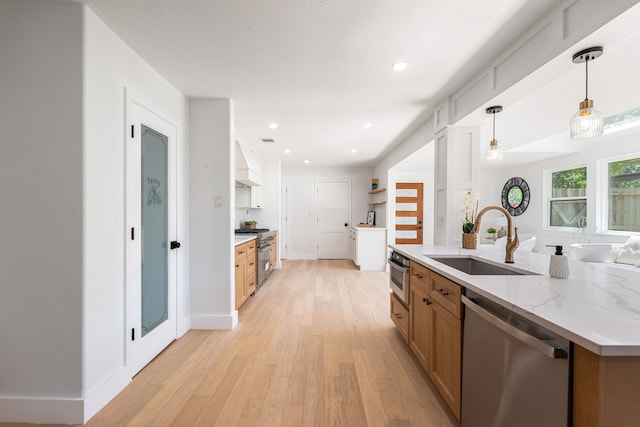 kitchen with appliances with stainless steel finishes, a sink, light wood finished floors, decorative light fixtures, and custom range hood