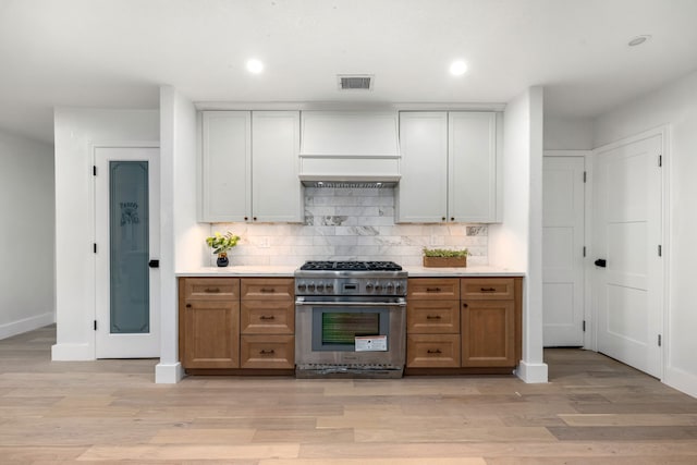 kitchen with light countertops, high end stove, baseboards, tasteful backsplash, and visible vents