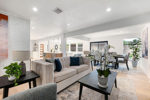 living area with light wood-type flooring, decorative columns, recessed lighting, and visible vents