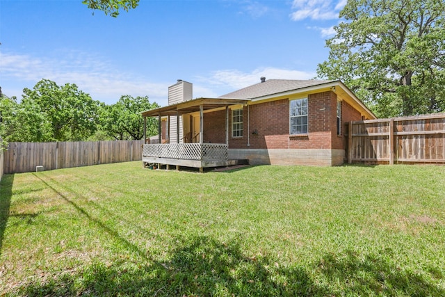 rear view of property with brick siding, a deck, a fenced backyard, a chimney, and a yard