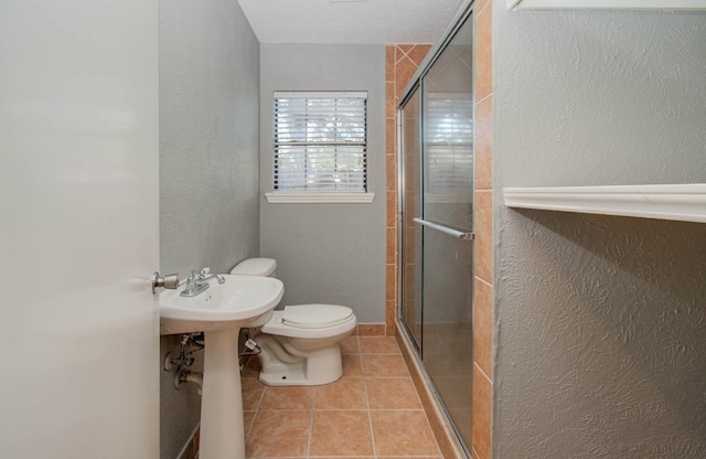bathroom featuring tile patterned floors, a textured wall, a stall shower, and toilet