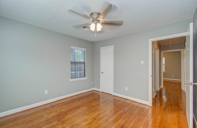 unfurnished bedroom with ceiling fan, a textured ceiling, light wood-style flooring, attic access, and baseboards