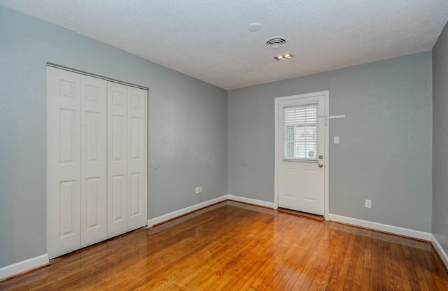 unfurnished bedroom with visible vents, wood-type flooring, baseboards, and a closet
