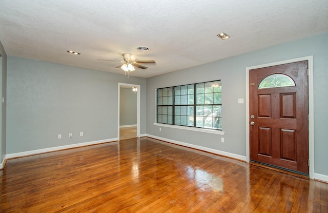foyer entrance with baseboards, a ceiling fan, wood finished floors, and visible vents