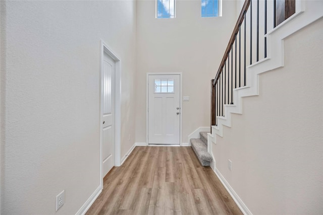entrance foyer featuring light wood-style floors, baseboards, a high ceiling, and stairway