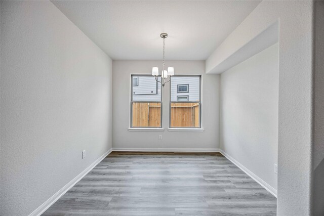 unfurnished dining area with baseboards, wood finished floors, and a chandelier