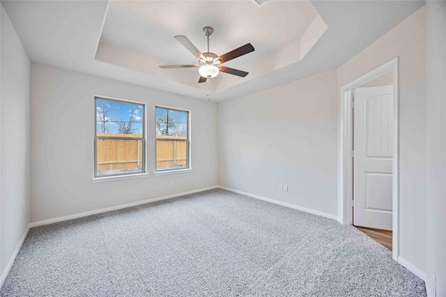 empty room featuring baseboards, carpet flooring, a raised ceiling, and a ceiling fan