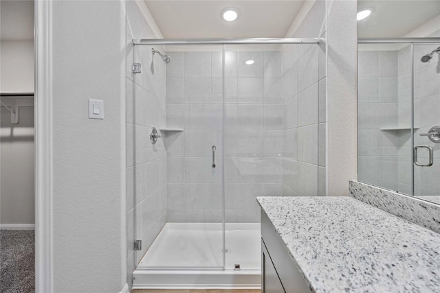 full bathroom featuring vanity, recessed lighting, a textured wall, and a shower stall