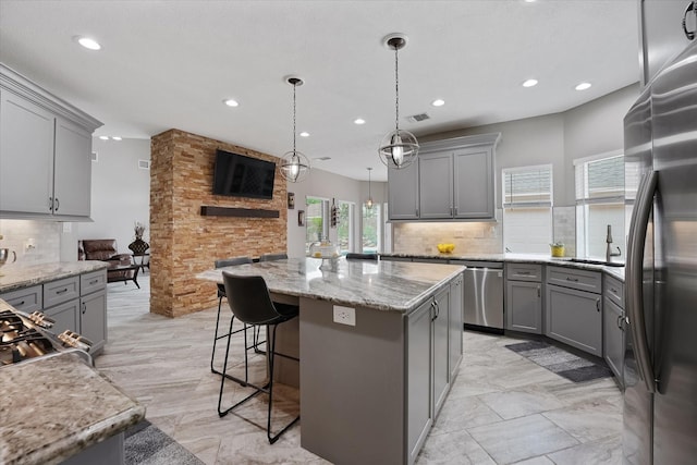kitchen featuring gray cabinets, appliances with stainless steel finishes, a kitchen island, and tasteful backsplash