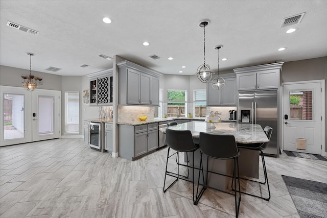 kitchen with visible vents, decorative backsplash, beverage cooler, gray cabinetry, and stainless steel appliances