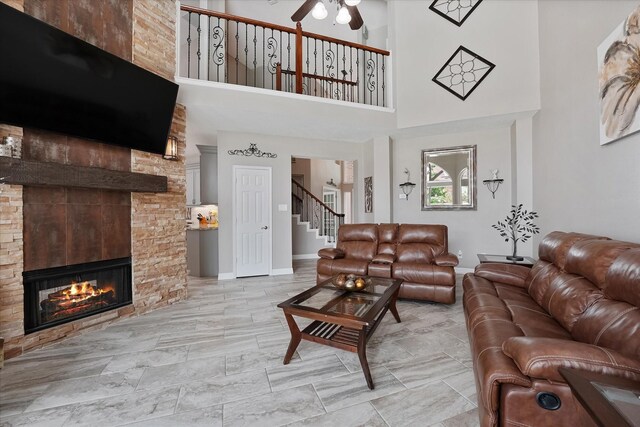 living area with ceiling fan, a high ceiling, a large fireplace, stairs, and baseboards