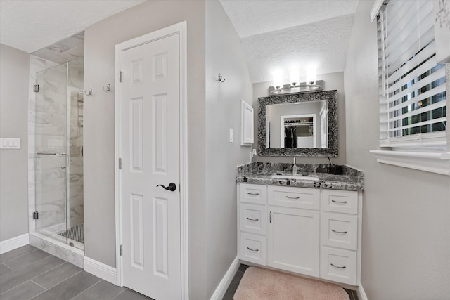 full bath with vanity, baseboards, a shower stall, and a textured ceiling
