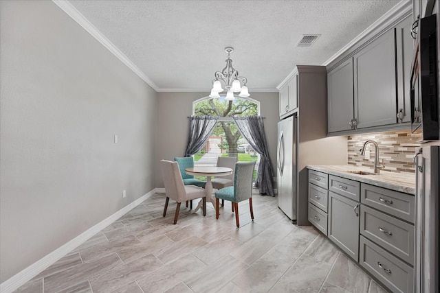dining space with a textured ceiling, a chandelier, baseboards, visible vents, and ornamental molding