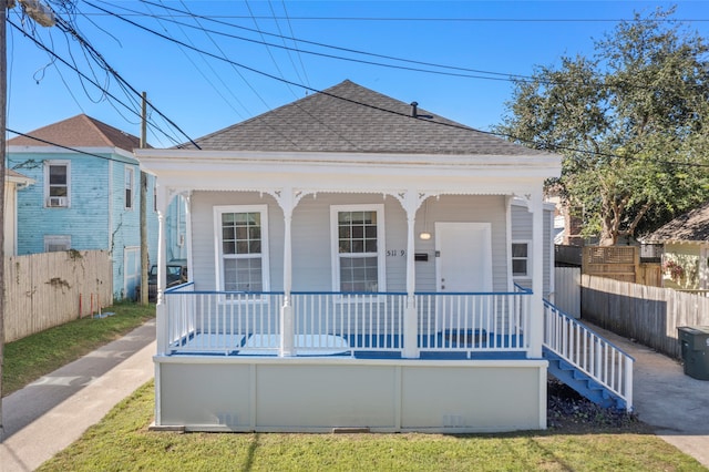 view of front facade with a porch, fence, and roof with shingles