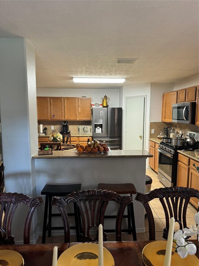 18207 Sea Branch Dr, Houston, TX 77084 - kitchen featuring a kitchen bar, visible vents, appliances with stainless steel finishes, tasteful backsplash, and a peninsula