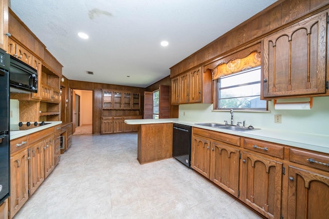 kitchen with a sink, light countertops, brown cabinetry, a peninsula, and black appliances