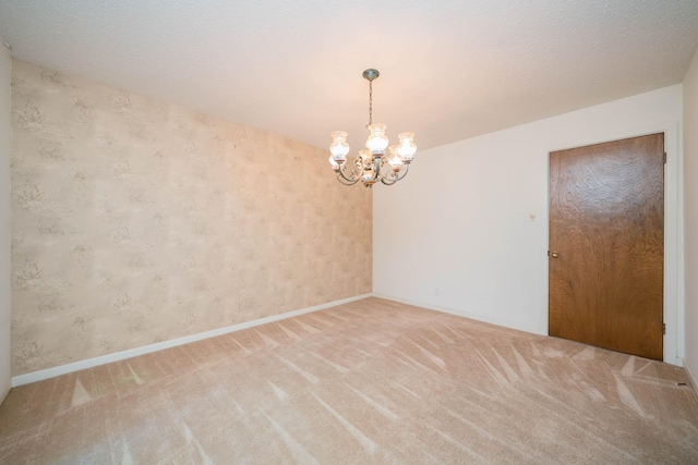spare room featuring baseboards, light carpet, wallpapered walls, and a chandelier