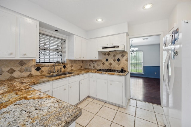 kitchen with a sink, under cabinet range hood, white cabinets, and freestanding refrigerator
