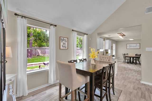 dining room featuring baseboards, visible vents, light wood finished floors, and lofted ceiling