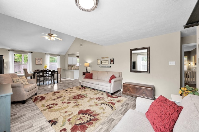 living room with light wood-type flooring, baseboards, ceiling fan, and vaulted ceiling