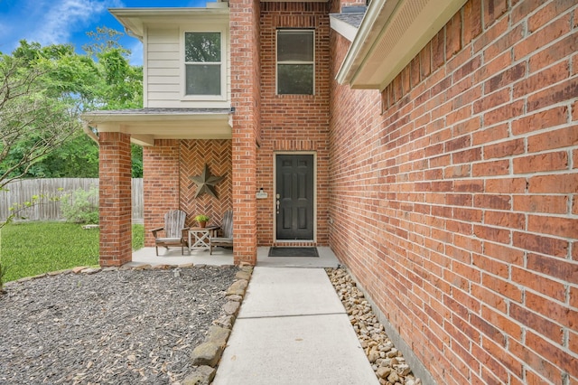 view of exterior entry featuring brick siding and fence
