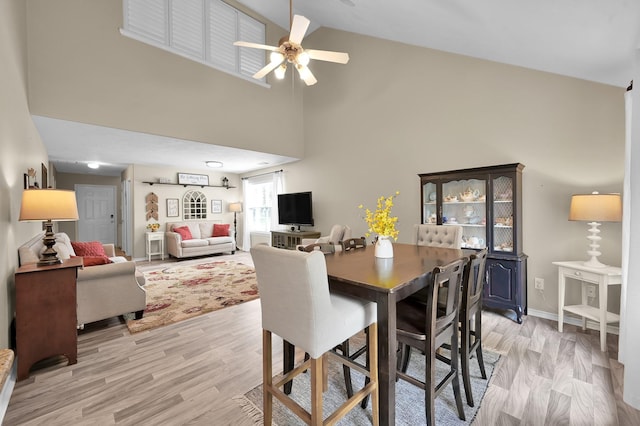 dining room with baseboards, ceiling fan, light wood-style flooring, and high vaulted ceiling