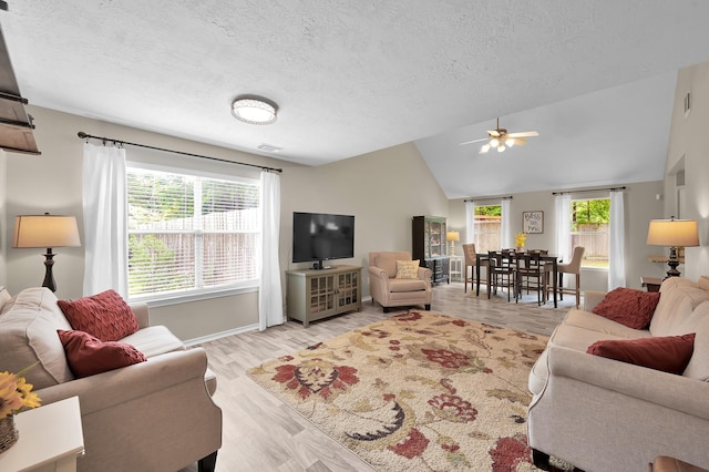 living room with ceiling fan, visible vents, light wood-style floors, a textured ceiling, and vaulted ceiling