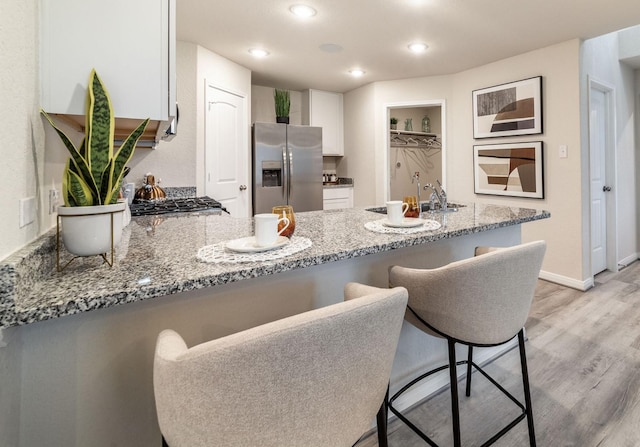 kitchen with white cabinets, light stone countertops, stainless steel fridge, a sink, and a peninsula