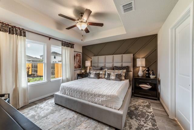 bedroom with ceiling fan, visible vents, wood finished floors, baseboards, and a tray ceiling