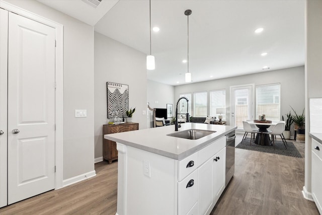 kitchen with a center island with sink, light wood-type flooring, dishwasher, a sink, and light countertops