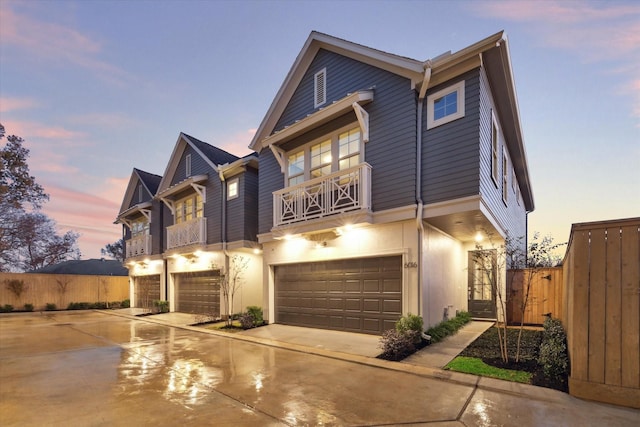 view of front facade with an attached garage, a balcony, fence, and driveway