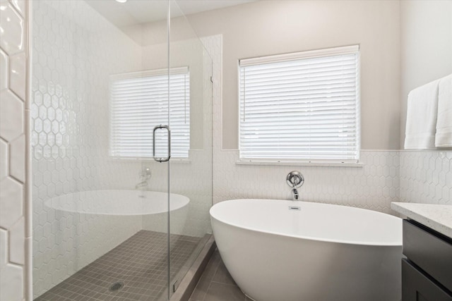 full bathroom featuring tile patterned flooring, wainscoting, a stall shower, vanity, and a soaking tub