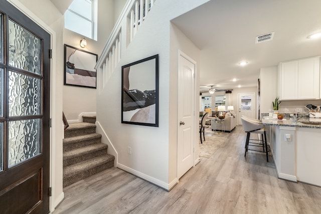 foyer featuring light wood-style flooring, stairs, a ceiling fan, baseboards, and visible vents